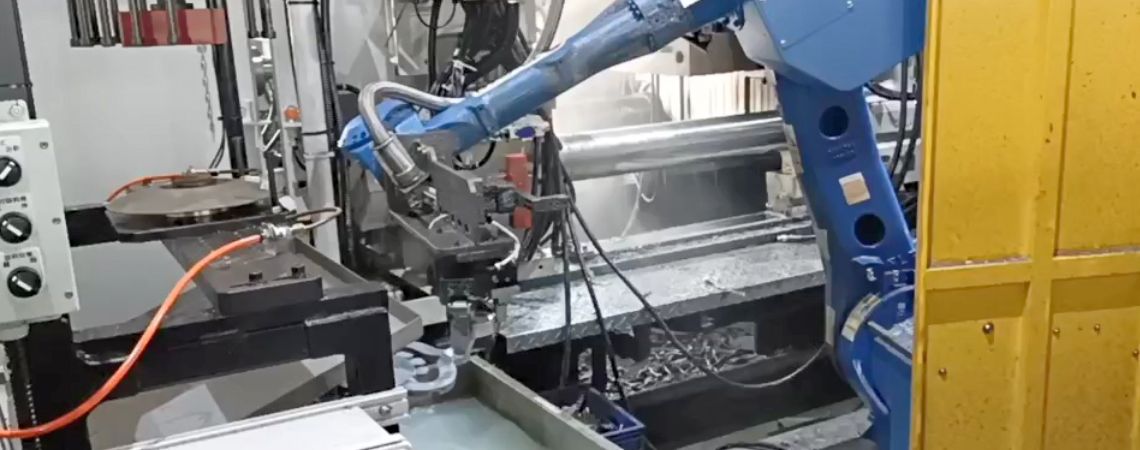Il braccio robotico YASKAWA GP50 posiziona il getto nella vasca di raffreddamento per ridurre la temperatura, con la macchina di rifilatura installata sopra la vasca.